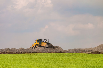 Yellow motorized bulldozer raking rubble piles. Road building industry.