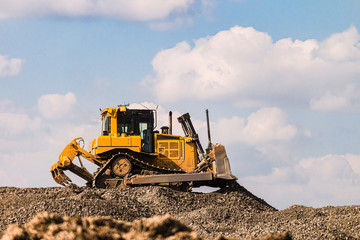 Yellow motorized bulldozer raking rubble piles. Road building industry.