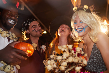 Low angle view at group of friends enjoying Halloween party in nightclub, focus on smiling young...