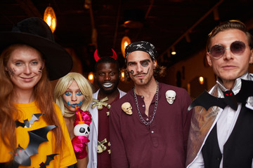 Multi-ethnic group of people wearing Halloween costumes posing looking at camera while enjoying party in nightclub