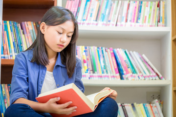 Portrait of clever student with open book reading it in college library