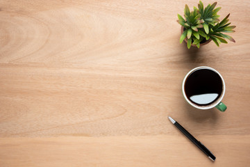 Wooden office desk table with cup of black coffee, pen and plant pot. Top view with copy space,...