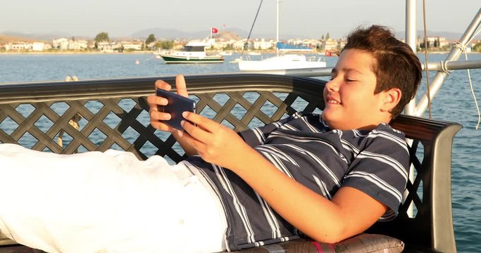 Portrait of a happy teenager boy on yacht deck taking selfie from smart phone at summer vacation. Travel, holiday, people, technology concept