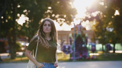 Portrait of a young serious woman with long beautiful hair in park during beautiful sunset