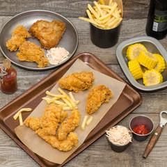 Dinner table with fried chicken, wings and strips, french fries, coleslaw and sauces. Homemade southern fried chicken. 