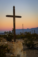 Cross in graveyard in the desert at sunset