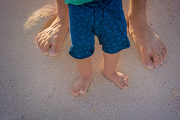 Feet of dad and son in the sand close up