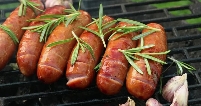 Grilling sausages with the addition of rosemary and garlic on the grill plate, top view, 4k. Grilling food, bbq, barbecue