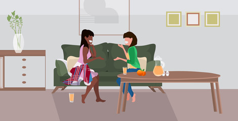 Fototapeta premium two girls sitting on couch mix race women couple discussing during meeting modern living room interior flat full length horizontal