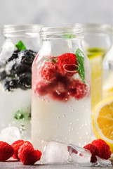 Berry and citrus soft drinks and cocktails in glass bottles on gray stone table background, copy space
