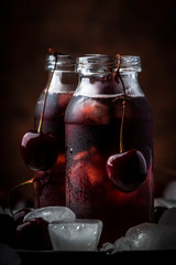 Cherry juice, cold beverage with ice in glass bottles on vintage wooden table, low key, copy space