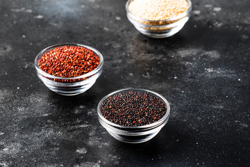 Black, white and red quinoa in bowls, raw quinoa groats set on gray kitchen table, copy space, selective focus