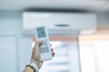 hand using remote controller for adjust Air conditioner inside the room of office or house