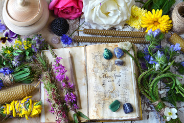 Witch spell book, calendula, rose flowers, reiki crystals and candles on wooden table.