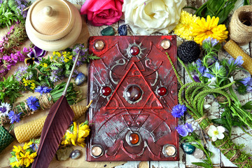 Decorated magic book, quill, summer herbs and flowers on witch table.