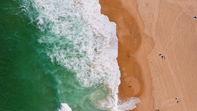 Top aerial view of waves break on tropical yellow sand beach. Bird's eye perspective of emerald green ocean surface and tourist relaxing on holiday