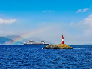 View of the Beagle Channel near Ushuaia, Argentina, where there is a small island with a popular tourist attraction, a lighthouse on a small island . A cruise ship and a rainbow are in the background.