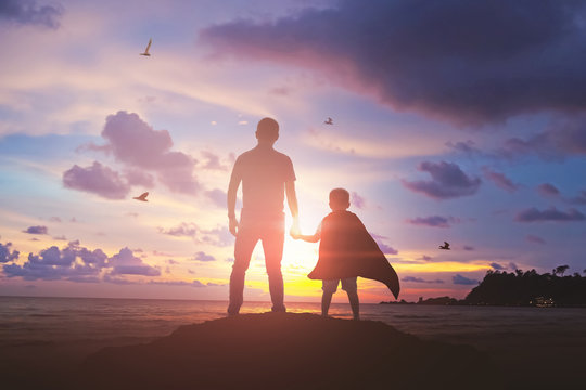 Super Son holding hand of fatheroutdoors on background sunset. Father holiday
