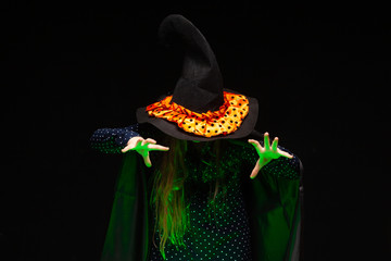 Halloween Witch over a pot of green glowing liquid conjures hands on black background. Beautiful young surprised woman in witches hat and costume . Wide Halloween party art design. Copy-paste. Witch