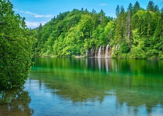 A beautiful summer nature scene in the forest, with waterfalls and trees reflected in a calm lake. Plitvice Lakes National Park, Croatia.