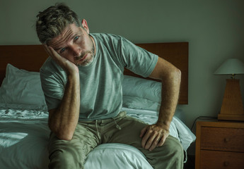 Fototapeta premium dramatic lifestyle portrait of 30s to 40s handsome man sitting sad on bed feeling worried and desperate suffering depression problem