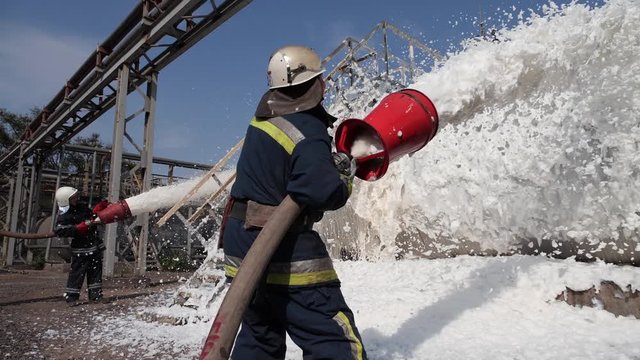 Three firefighters extinguish a fire at a tank farm with foam