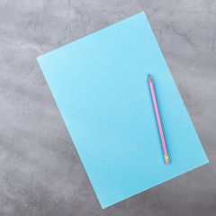 Flat lay, top view, blue sheet and pencil on a gray textured background. Rays of light from the side.