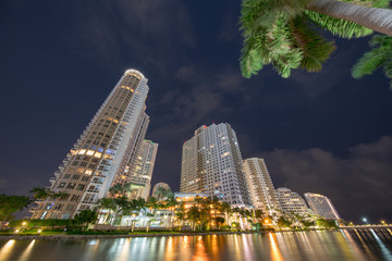 Brickell Key Miami highrise condominiums. Long exposure photo shot at night with blurry clouds and palm trees. Water smooth surface