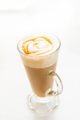 Hot caramel macchiato in a tall glass with caramel sauce on top close up.