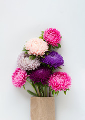 Beautiful colourful asters bouquet packed in craft paper on light gray background.