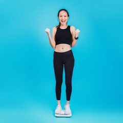 Asian beautiful woman feeling happy and standing on the Weight Scale at blue color background.Concept of weight loss for good health with excercise.