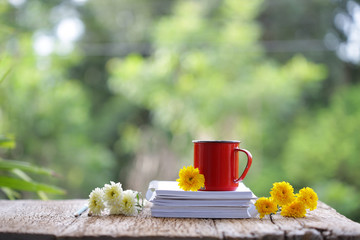 Red coffee mug with Chrysanthemum flowers and notebooks on wooden table at outdoor