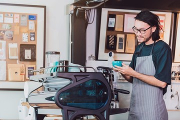 Young Asian man barista wear apron holding coffee cup served to customer at bar counter in coffee shop with smile face.Concept of cafe and coffee shop small business.Vintage tone