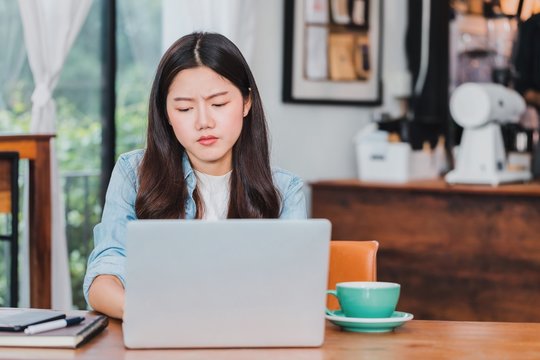 Asian beautiful young businesswoman feeling worry and stress in coffee shop and cafe background with laptop and coffee cup on wood table.Concept of inconvenience to use online technology.