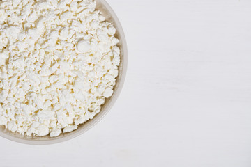 bowl of fresh farm cottage cheese on a white wooden background, top view