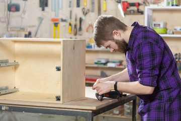 Young bearded man working at the furniture factory