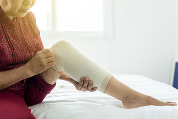 Senior asian woman using elastic bandage on injured knee