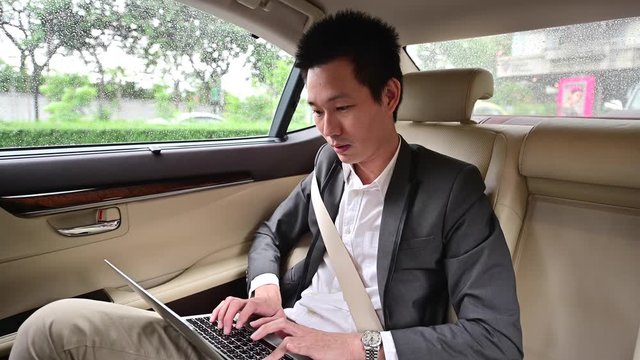 4K Young businessman using laptop in back seat of car