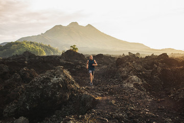Young athlete man trail running in mountains in the morning. Amazing volcanic landscape of Bali mount Batur on background. Healthy lifestyle concept.