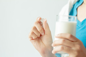 Woman hand holding pill and glass of milk on white background. Do not eat at the same time.