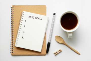 Text 2020 goals on notebook with pen on white background,office desk.