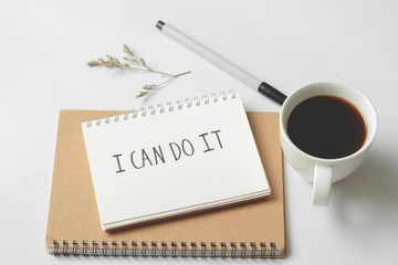 Written words "I can do it" on paper notebook with coffee and pen on white desk background.