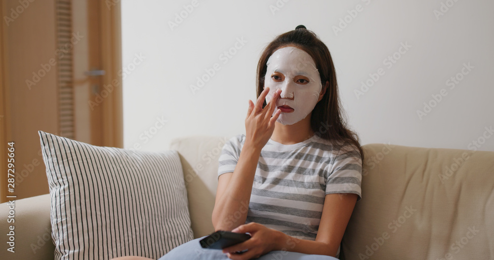 Poster Woman apply paper mask on face and watch tv at home