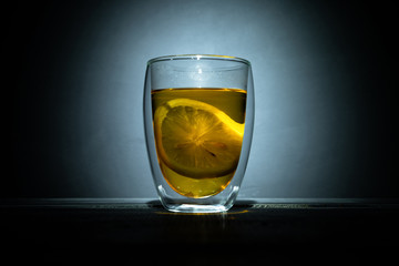 black tea with slice lemons in glass thermomug on dark background in spot light