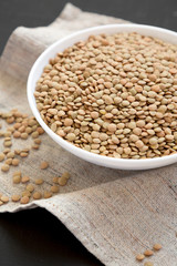Organic green lentils in a white bowl on a black surface, side view. Close-up.
