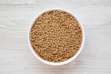 Organic green lentils in a white bowl on a white wooden background, top view. Flat lay, overhead, from above. Close-up.