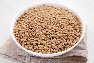 Organic green lentils in a white bowl on a white wooden background, low angle view. Close-up.