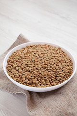 Organic green lentils in a white bowl on a white wooden surface, low angle view. Copy space.