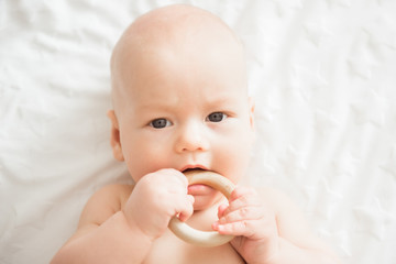 Cute newborn baby takes a wooden toy in his mouth. Teething and health concept
