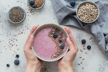 Woman's Hands holding pink yogurt smoothie bowl made with fresh berry and seeds